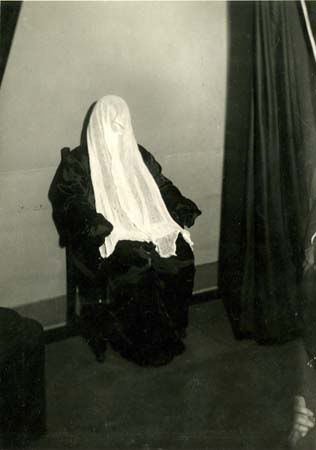 A photograph of medium Helen Duncan during a seance with head covered ...